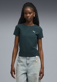 Mørkegrøn bomulds t-shirt med korte ærmer og rund halsudskæring, med et hvidt Puma-logo på brystet. Bæret med lyse denim jeans.