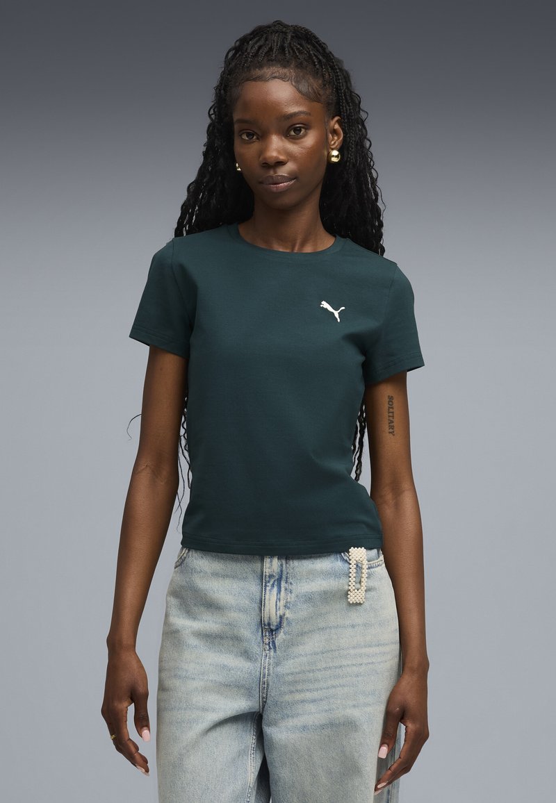 Mørkegrøn bomulds t-shirt med korte ærmer og rund halsudskæring, med et hvidt Puma-logo på brystet. Bæret med lyse denim jeans.
