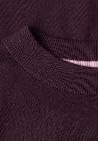 Gros plan sur l'encolure d'un pull tricoté violet foncé avec un col côtelé et un aperçu d'une couche intérieure rose clair.