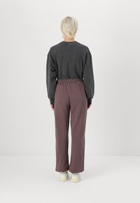 Siva oversize majica s padlim ramenima, uparena s labavim tamnoplavim trenirkama koje imaju elastičan pojas, i bijelim tenisicama.