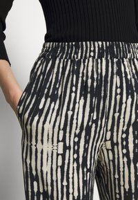 Černé a krémové vzorované kalhoty s elastickým pasem a bočními kapsami, s vertikálními pruhy a měkkou tkaninou.