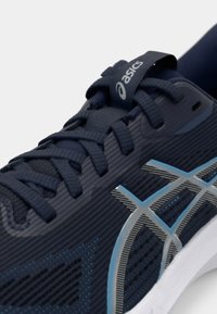 Granatowe buty biegowe z teksturowaną siateczką, szarymi akcentami i białą podeszwą. Posiadają zaokrąglone sznurówki oraz metkę z logo na języku.