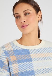 Maglione lavorato a maglia con scollo rotondo, caratterizzato da un motivo a quadri diagonali blu, crema e pesca. Texture morbida, design che si adatta comodamente.