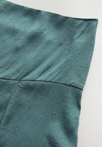 Tessuto in tono teal, liscio con una superficie stropicciata, ripiegato nella parte superiore con una cucitura pulita. Leggermente riflettente e si drappeggia dolcemente.