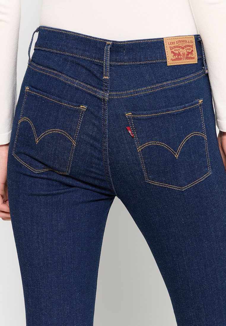 Rückansicht einer Person, die dunkelblaue Levi's-Jeans mit sichtbaren Gesäßtaschen, Nähten und einem Markenlabel am Bund trägt.
