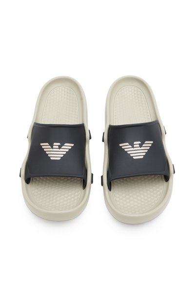 Infradito nere in gomma con una soletta in crema testurizzata, caratterizzate da un logo argento prominente sulla fascia. Design durevole e resistente all'acqua.