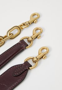 Gold hardware clips are attached to a dark burgundy leather strap featuring stitching details and smooth texture, arranged in a flat layout.