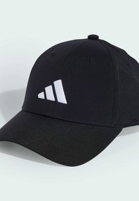 Black cap made of fabric with a curved brim. Features a white three-stripe logo on the front. Includes ventilation holes and a rounded top.