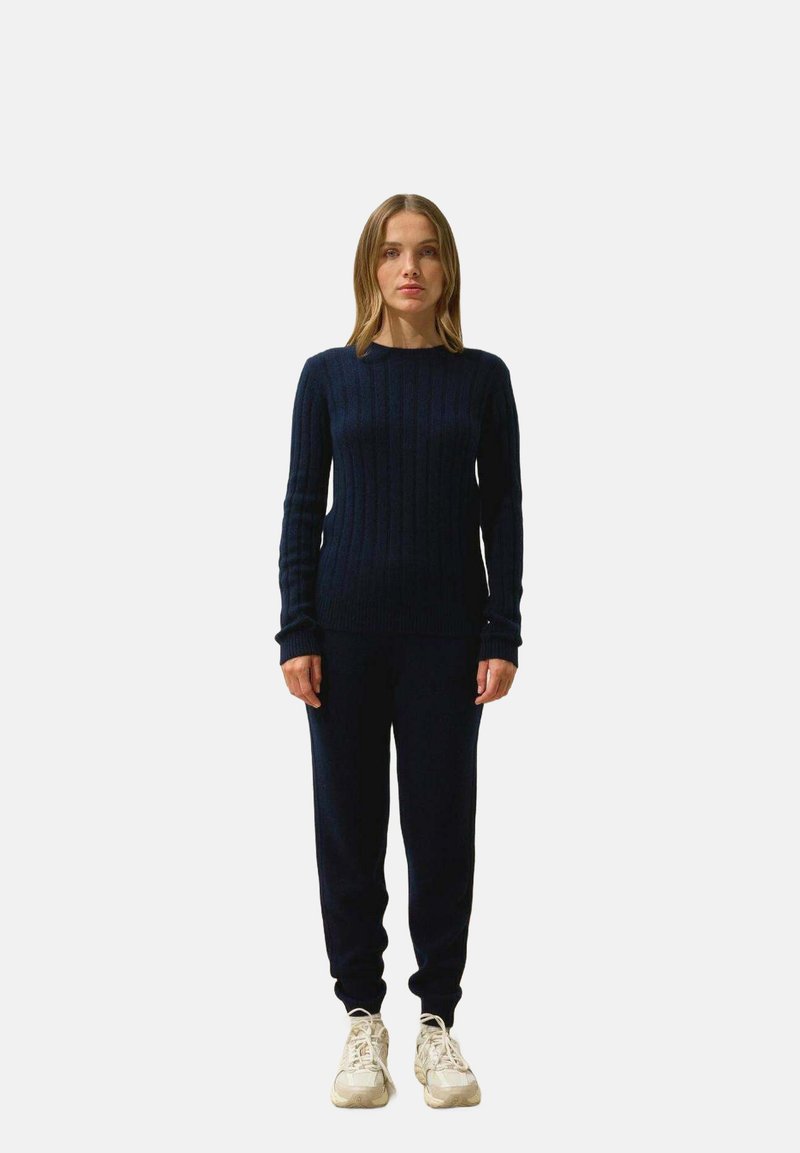 Pull en tricot côtelé bleu marine à manches longues associé à un jogging assorti. Porté avec des baskets claires. Design ajusté et texture douce.