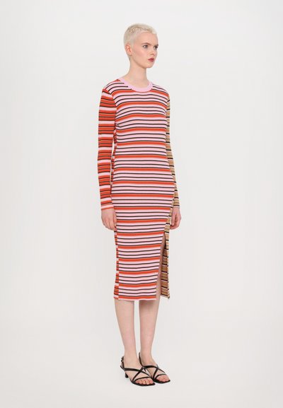 Gestreiftes Langarmkleid in rot, pink und beige aus Rippstrick. Mit einem seitlichen Schlitz und kontrastierendem Farbschema an den Ärmeln. Schwarze Sandalen mit Riemchen.