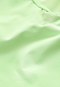 Light green fabric with a smooth texture, featuring a subtle sheen and a mesh accent detail near the neckline.