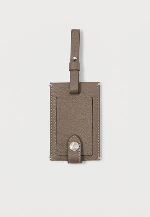 Etichetta per bagagli in pelle di un colore taupe scuro con una finitura testurizzata, dotata di un attacco a loop e un dettaglio in metallo argentato a pressione. Slot per due carte visibili.