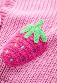 Rózsaszín kötött ruhadarab, amelyen jól láthatóan hímzett, texturált eper applikáció található zöld levelekkel és a gyümölcsön több színű pöttyökkel.