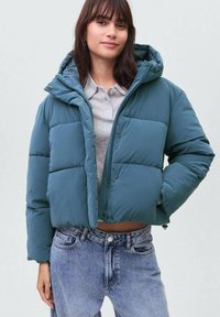 Tmvattna puffer jakna z značilnim krojem, s kapuco in zapiranjem na gumbi. Narejena iz gladkega, podloženega materiala z izrazitimi šivi.