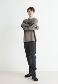 Šviesiai pilka mezgimo megztinis su juodais siuvinėjimo akcentais ant rankovių, derinamas su tamsiai pilkomis kelnėmis ir juodais kulkšninių botais. Minimalistinis dizainas.