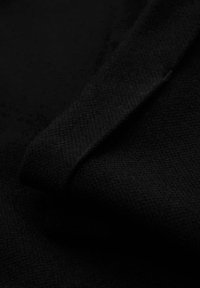 Gros plan d'un tissu noir texturé plié en diagonal, mettant en évidence son motif de tricot fin et sa surface douce.