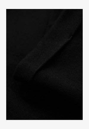 Gros plan d'un tissu noir texturé plié en diagonal, mettant en évidence son motif de tricot fin et sa surface douce.