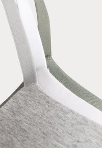 Šedá tkaninová podprsenka s měkkou strukturou, která má bílé a světle zelené nastavitelné ramenní popruhy. V místě spojů jsou viditelné švy.