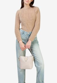 Beige striktrøje med ribbet tekstur, parret med lyseblå højtaljede jeans. Modellen holder en blød, lys beige håndtaske med guld accenter.
