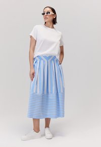 Biała koszula z krótkim rękawem w połączeniu z niebieską, w paski, plisowaną maxi spódnicą z poziomymi i pionowymi paskami. Uzupełniona białymi trampkami.