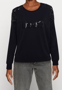 Sudadera negra con acentos de lentejuelas en los hombros y el logo "LIUJO" en la parte frontal. Presenta puños y bajo acanalados. Tejido suave y texturizado.