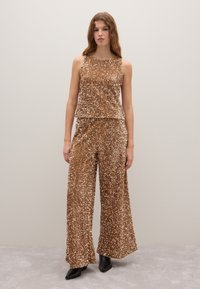 Zweiteiliges Outfit mit Pailletten in metallic Braun; ärmelloses Oberteil mit lässigem Schnitt, weit geschnittene Hose mit Falten und glatter Textur, kombiniert mit schwarzen Stiefeln.