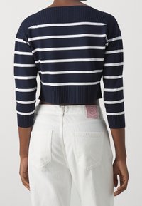 Maglione cropped a righe blu navy e bianche con maniche a tre quarti e scollo a costine. Jeans bianchi a vita alta con tasche posteriori.
