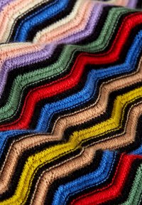 Wielokolorowa dzianina z wzorem w zygzak w kolorach czerwonym, niebieskim, zielonym, czarnym, różowym i żółtym. Miękka tekstura z wyraźnymi paskami kolorów.