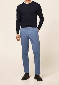 Námořnický pletený svetr s dlouhými rukávy, kombinovaný se světle modrými slim-fit kalhotami a černými kotníkovými botami, které ukazují hladkou texturu a střih.
