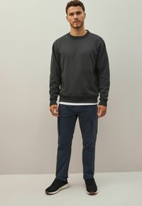 Mörkgrå sweatshirt med rund hals, kombinerad med marinblå cargobyxor med sidofickor och svarta sportskor. Enkel, avslappnad outfit.