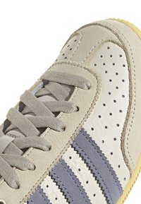 Grå och vit sneaker med texturerad mocka och slät läder, med perforeringar, grå ränder och en gummisula.