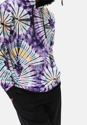 Sudadera con capucha con patrones espirales tie-dye en morado, amarillo y verde azulado, puños negros, bolsillo delantero y logo de Vans en el pecho, combinado con pantalones negros.