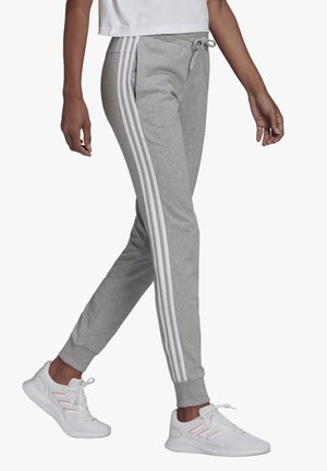 Personne marchant portant un jogging gris avec des bandes blanches sur le côté et des baskets blanches avec des accents roses.