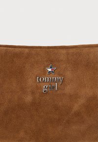Brūna zamšādas soma ar sudraba toņa "tommy girl" logo un zvaigžņu akcentu. Gluda tekstūra ar minimālistisku dizainu.