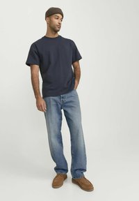 Marineblaues Rundhals-T-Shirt mit kurzen Ärmeln, kombiniert mit hellblauen geraden Jeans und braunen Slippern. Einfaches, lässiges Design.