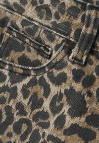 Leopardmönstrad tyg med en blandning av brunt och svart. Närbild visar sömmar och en fickdetalj med en strukturerad denimliknande yta.