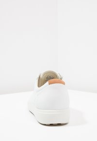 Hvit sneaker med en glatt skinnfinish, med en beige aksent på hælen. Rund form med en myk, polstret såle.
