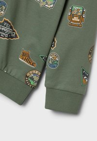 Sudadera verde con varios parches de temática al aire libre en colores vivos, con texto, puños acanalados y una textura de tela suave.