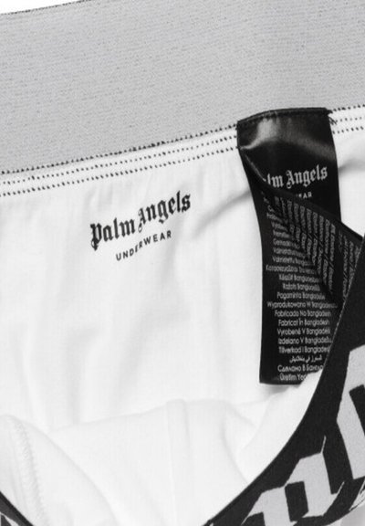 Λευκά εσώρουχα Palm Angels με γκρι ζώνη μέσης και μαύρη ετικέτα που δείχνει το όνομα της μάρκας και οδηγίες φροντίδας σε πολλές γλώσσες.