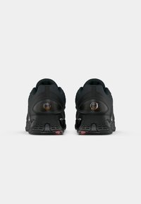 Black athletic shoes with textured mesh upper, padded collar, and rubber sole featuring red accents. Rear view shows logo and distinct tread pattern.