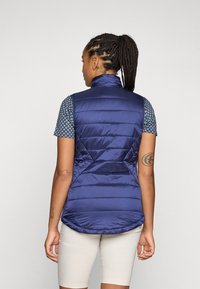 Marineblauer Puffer-Weste mit hohem Kragen, gestepptem Design und schlanker Silhouette; kombiniert mit einem gemusterten kurzärmligen Oberteil.