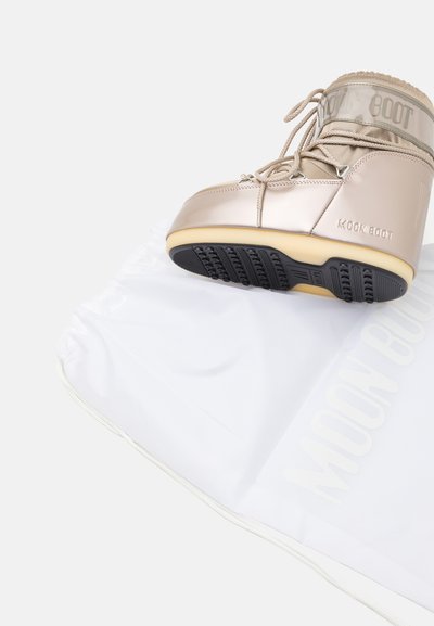 Metallic beige Moon Boot with a padded upper, lace closure, and rubber sole. Accompanied by a white drawstring storage bag.