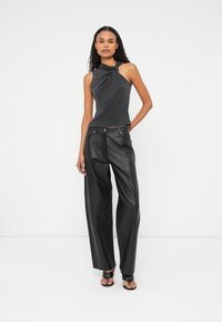 Zwarte mouwloze top met een gedraaide ontwerp, gecombineerd met brede zwarte leren broek, met een gladde textuur en minimale hardware.