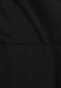 Černá tkanina s hladkým, mírně texturovaným povrchem, ukazující jemné záhyby. Šev probíhá horizontálně poblíž středu.