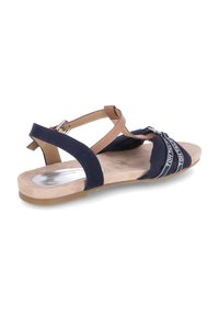 Sandal in blu navy con cinturini in suede e pelle, design aperto, suola piatta e un accento metallici con etichetta del brand sui cinturini.