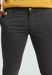 Pantalons gris foncé en tissu lisse, avec une fermeture à bouton à l'avant, des passants de ceinture et des poches latérales. Design ajusté avec une silhouette élégante.