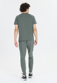 Miesten urheiluasu hillityssä vihreässä, joka koostuu lyhythihaisesta paidasta ja kavennetuista housuista, valmistettu kevyistä materiaaleista, yhdistettynä juoksukenkien kanssa.