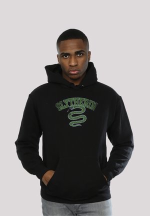 Svart hettegenser med "Slytherin"-tekst i grønt over et grønt slangegrafikk. Tøyet ser mykt ut, med en frontlomme og hette med snøring.