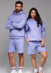 Fialová sada mikiny a šortek vyrobená z měkké tkaniny. Mikina má šňůrky; šortky mají elastický pas a boční kapsy.
