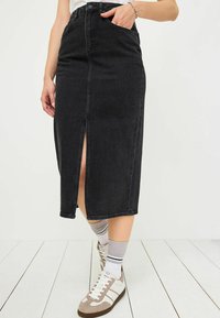 Svart denimpenskirt med en framklippt, hög midja, sidofickor och kontrasterande sömmar, matchad med vita och grå sneakers.
